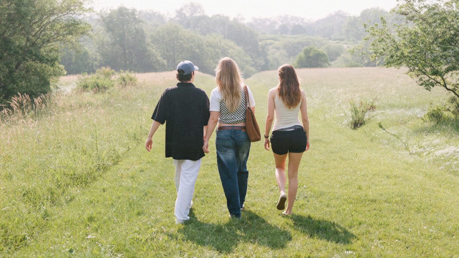 Three friends walking a sunlit meadow path together toward the morning light